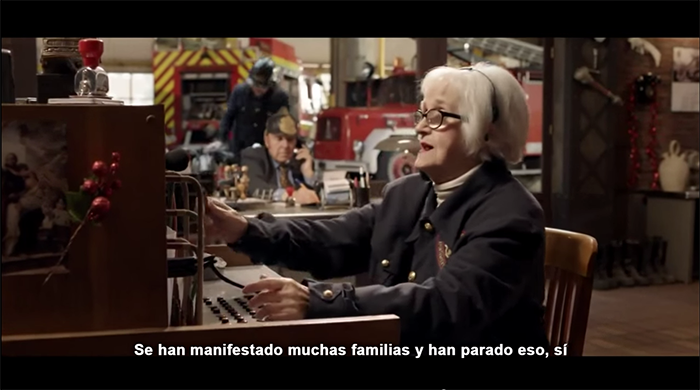 Fotograma del spot para TV de la campaña Bombería de Campofrío. Chus Lampreabe maneja una centralita de teléfonos con clavijas. En la parte inferior de la imagen, un subtítulo en blanco dice: “Se han manifestado muchas familias y han parado eso, sí”. En un segundo plano, Chiquito de la Calzada lleva un casco de bombero en la cabeza.